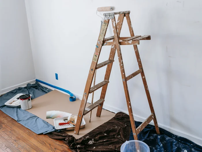 Room prepped for painting with drop cloths down, baseboards taped and a roller ready on the ladder
