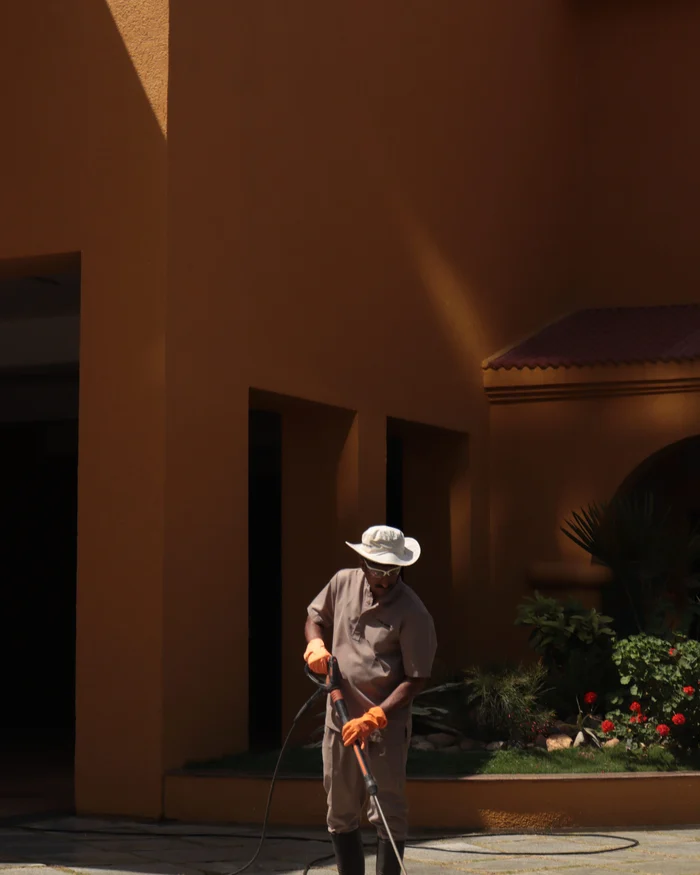 Worker pressure washing a stone walkway in front of a stucco building