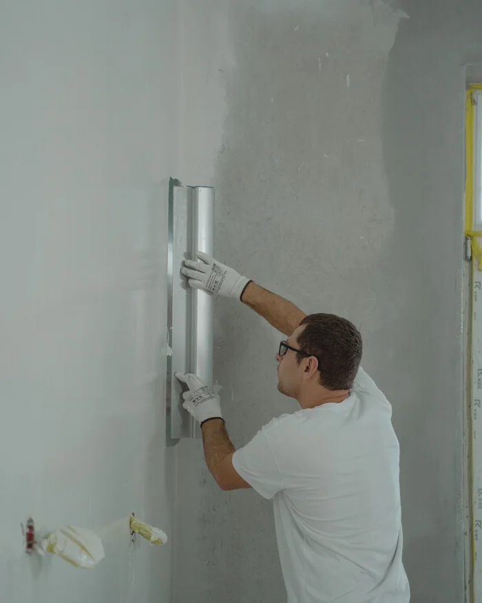 Painter skim coating a repaired wall smooth with a wide finishing blade